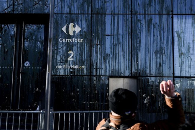 Un manifestant jette des oeufs sur la façade du siège du groupe Carrefour lors d'un rassemblement de producteurs d'oeufs, le 11 février 2022 à Massy, dans l'Essonne