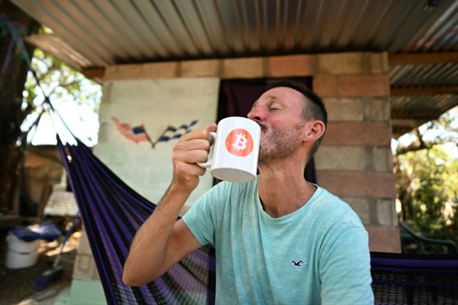 L'Américain Corbin Keegan boit dans un mug décoré du logo Bitcoin à Playa Blanca, le 11 janvier 2024 au Salvador