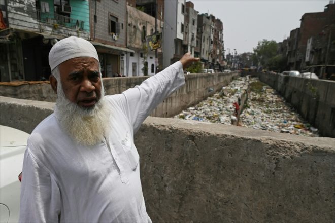 Un habitant de New Delhi, Khalil Ahmad, montre un égout pluvial rempli d'ordures dans le quartier de Seelampur, le 26 avril 2023
