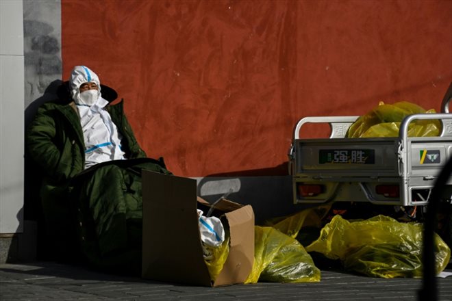 Un garde en combinaison de protection se protège du froid avec des vêtements chauds devant une zone résidentielle confinée en raison du Covid-19, à Pékin le 29 novembre 2022