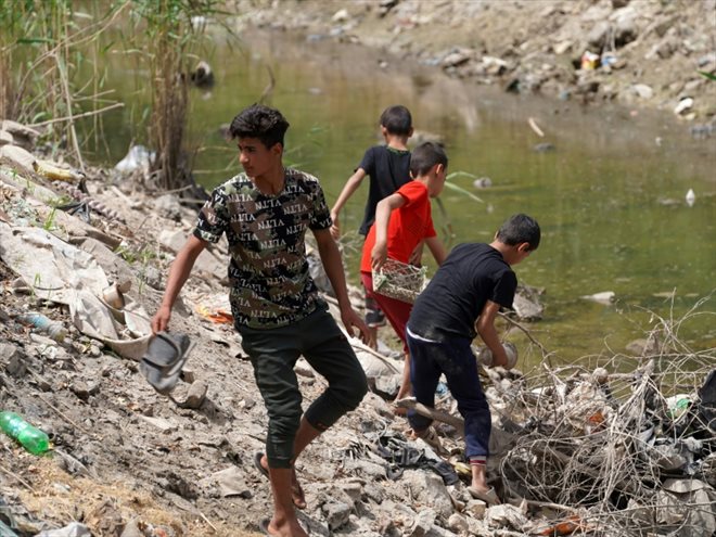 De jeunes Irakiens au bord d'une rivière polluée et assechée à Najaf, le 1er mai 2022