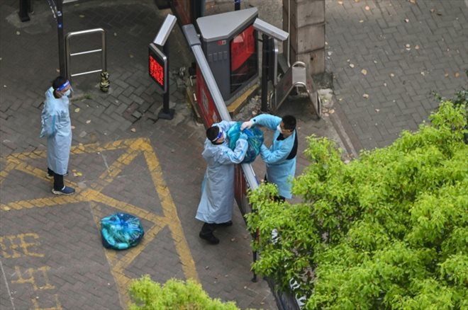 Un gardien portant des vêtements de protection reçoit des marchandises apportées par un livreur, lors du confinement, dans le quartier Jing'an de shanhai, le 8 avril 2022