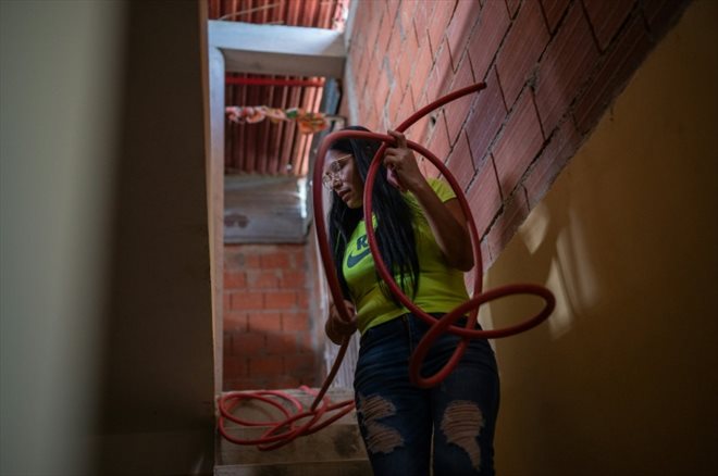 Yusmary Gomez tient un tuyau pour remplir d'eau le réservoir de sa maison dans le quartier de La Vega, à Caracas, le 9 août 2023 au Venezuela