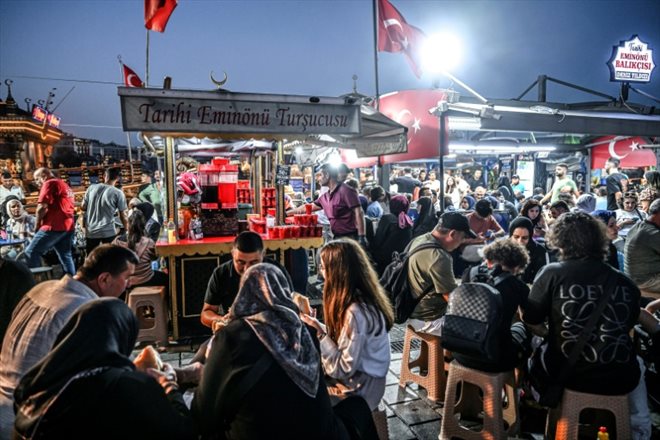 Un vendeur ambulant vend des légumes marinés derrière des gens attablés dans le quartier d'Eminonu à Istanbul, le 30 août 2024