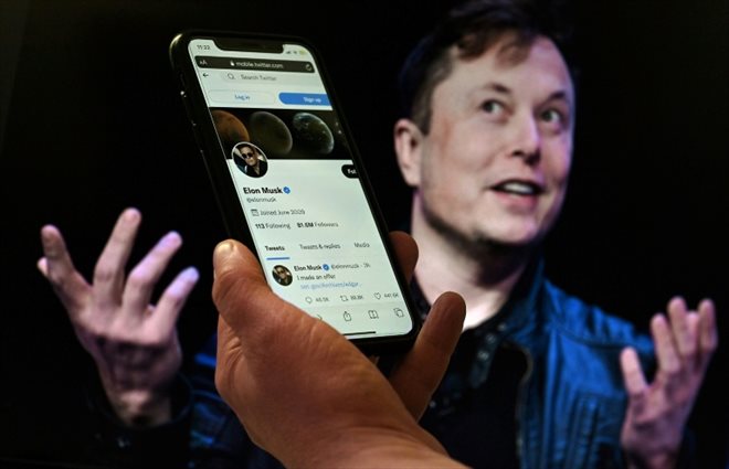 Une personne tient un téléphone affichant le compte Twitter d'Elon Musk devant une photo du patron de Tesla, le 14 avril 2022 à Washington