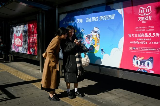 Deux habitantes de Pékin le 11 novembre 2023 devant une affiche faisant la promotion de la Fête des célibataires, grande opération de soldes en Chine qui s'achève cette année dans un contexte de consommation atone.