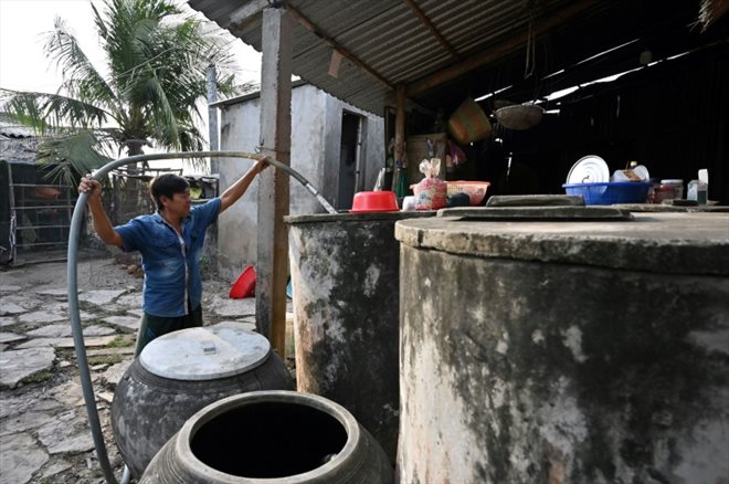 Un agriculteur remplit des réservoir d'eau fraîche achetée à un revendeur dans la province de Ben Tre, le 19 mars 2024 dans le sud du Vietnam