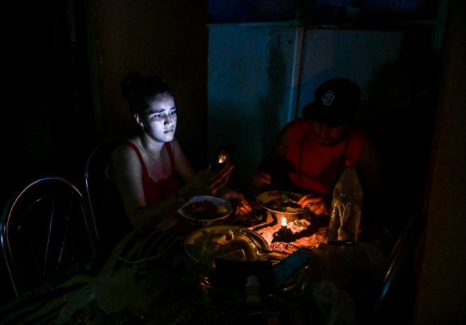 Une femme consulte son téléphone tout en dînant à la bougie pendant une coupure de courant, le 25 mai 2022 à La Havane