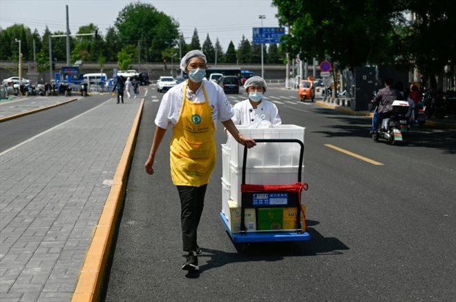 Des employés d'un restaurant poussent un chariot de plats à emporter dans une rue de Pékin, le 18 mai 2022