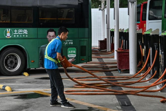 Un employé tient un câble de recharge d'un bus électrique dans une  station de recharge à Shenzhen, le 18 octobre 2023 dans le sud de la Chine
