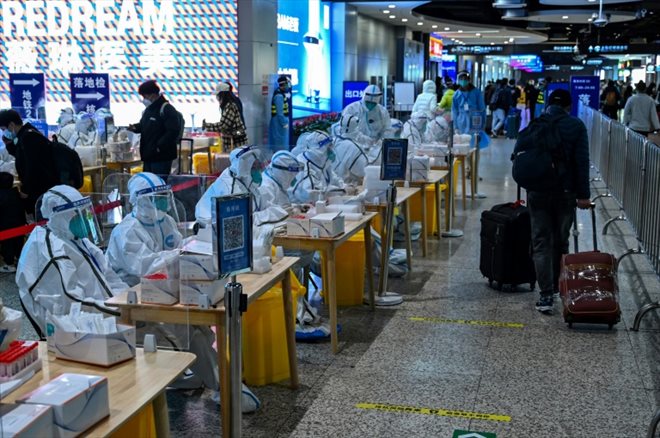 Des personnes en combinaison de protection attendent de tester les passagers pour le coronavirus Covid-19 après leur arrivée à la gare de Hongqiao à Shanghai, le 6 décembre 2022
