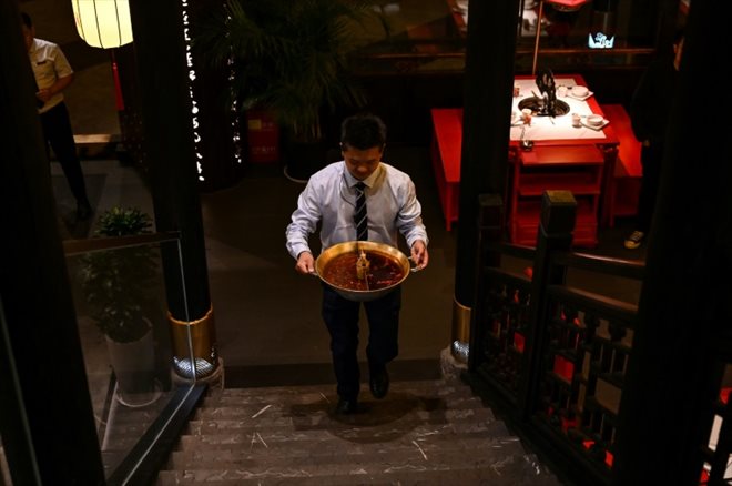 Un serveur emporte un pot de bouillon huileux, qui sera recyclé, dans un restaurant de fondue à Chengdu, dans la province du Sichuan, le 21 octobre 2023 en Chine