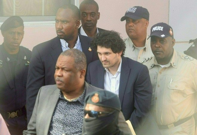 Le fondateur de FTX, Sam Bankman-Fried (centre), menotté, est accompagné par des agents de la police des Bahamas à Nassau (Bahamas) le 19 décembre 2022