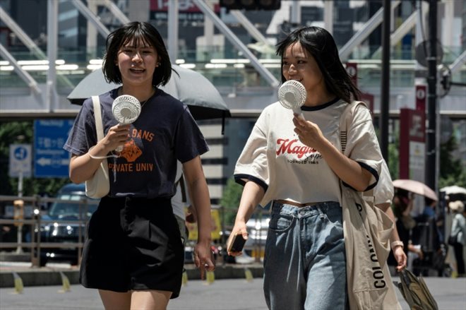 Deux jeunes femmes utilisent des ventilateurs portables pour se rafraîchir dans la rue lors d'un épisode de fortes chaleurs, le 30 juillet 2023 à Tokyo