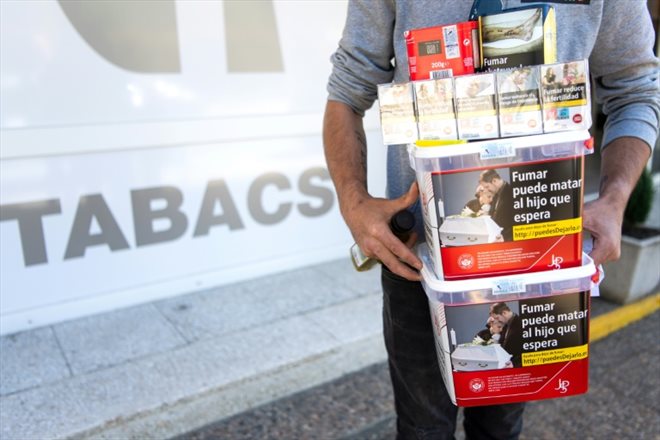 Un hommes porte des paquets de tabac achetéd dans une boutique de Les, en Espagne, le 19 avril 2024