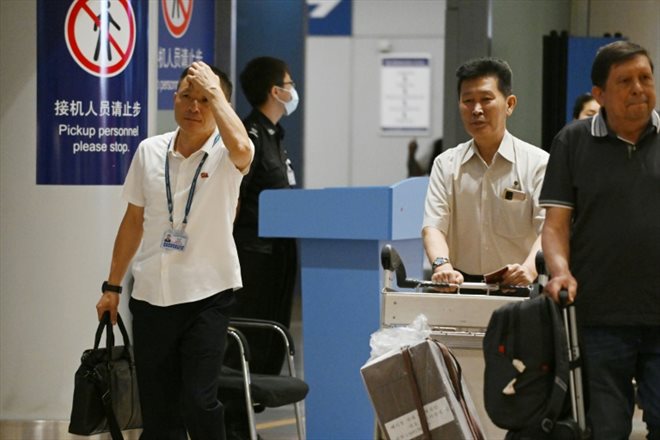 Deux hommes nord-coréens (à gauche et deuxième à droite) traversent la section des arrivées de l'aéroport de Pékin après l'arrivée du vol JS151 d'Air Koryo, le 22 août 2023